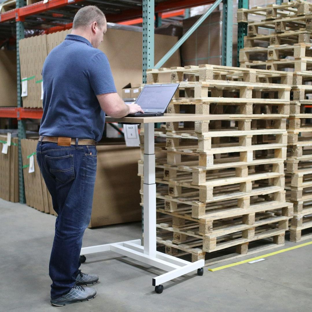 man in blue polo shirt and blue denim jeans standing near brown wooden shelf